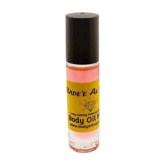 A bottle of Bade'e Al Oud body oil, pink color, with a yellowlabel and black cap, set against a white background.